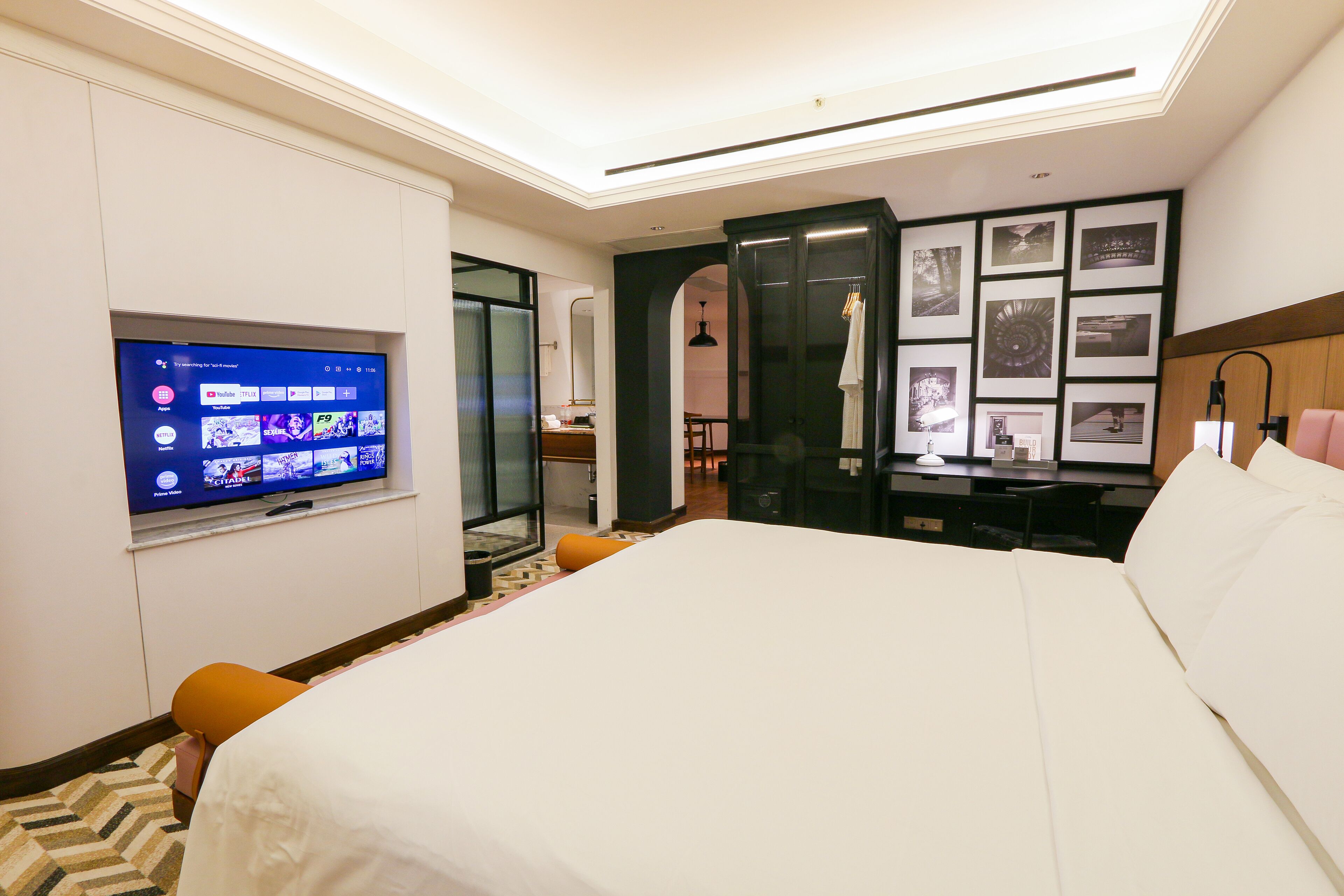 A hotel room with a bed, a desk, a television, and a wall with framed pictures.