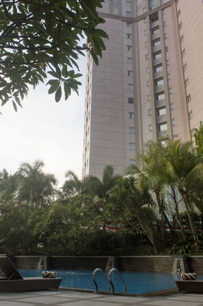 A high-rise building with a swimming pool and lounge chairs.
