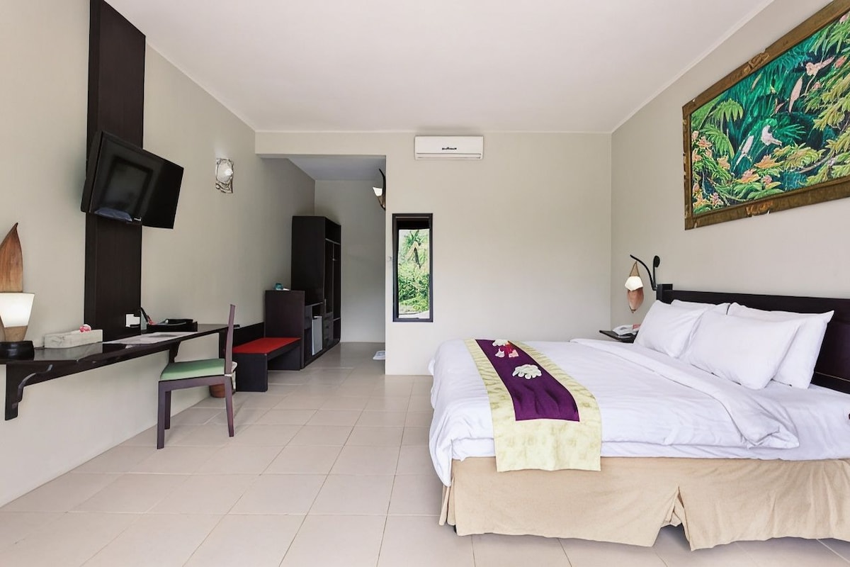 A hotel room with a bed, desk, chair, television, and a painting on the wall.
