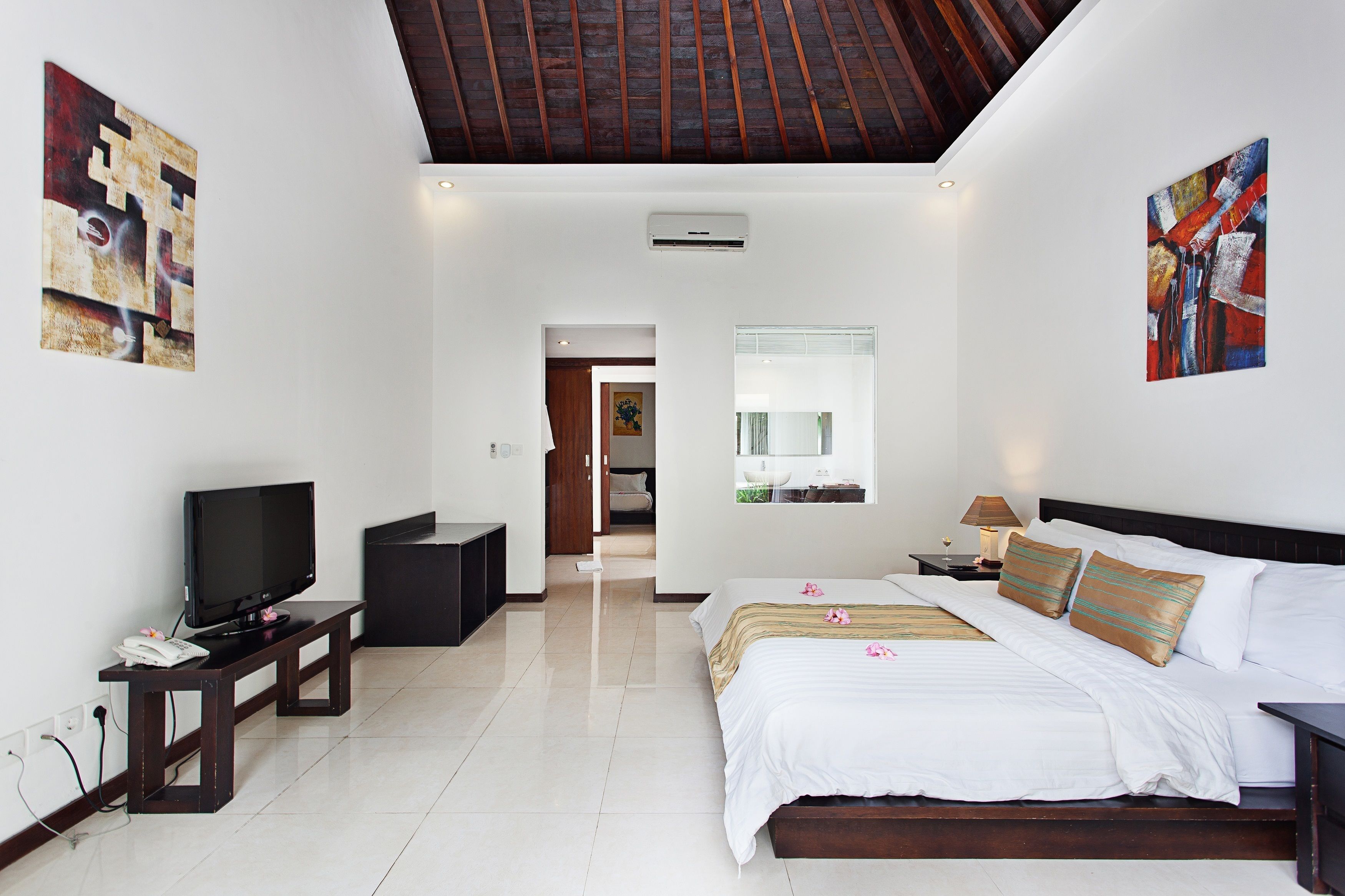 A modern hotel room with a large bed, a TV, a desk, and artwork on the walls.