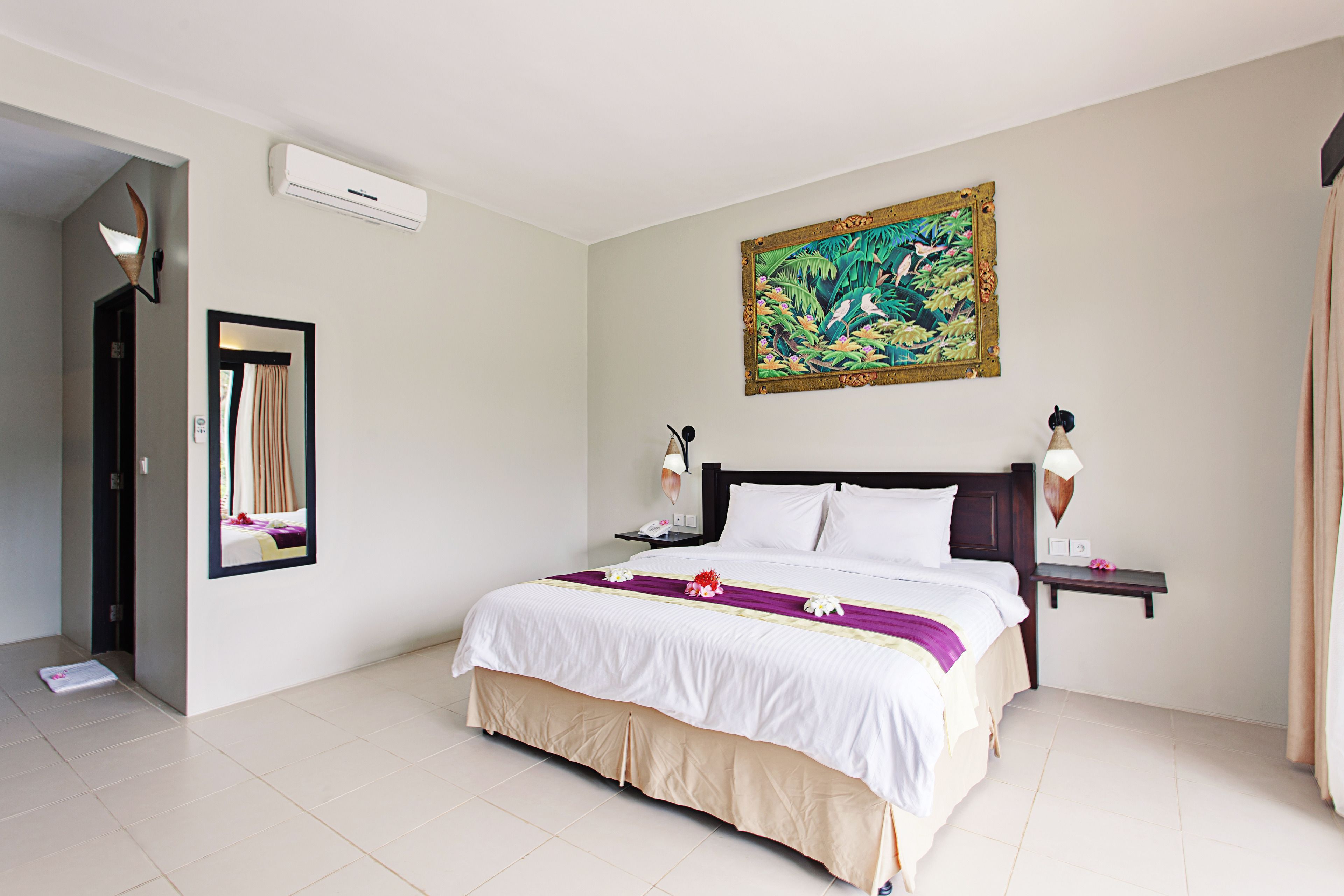 Una habitación de hotel con una cama grande, una mesita de noche, aire acondicionado montado en la pared, un cuadro y un espejo.