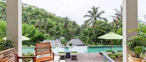 A wooden deck with a pool, surrounded by lush greenery and palm trees.
