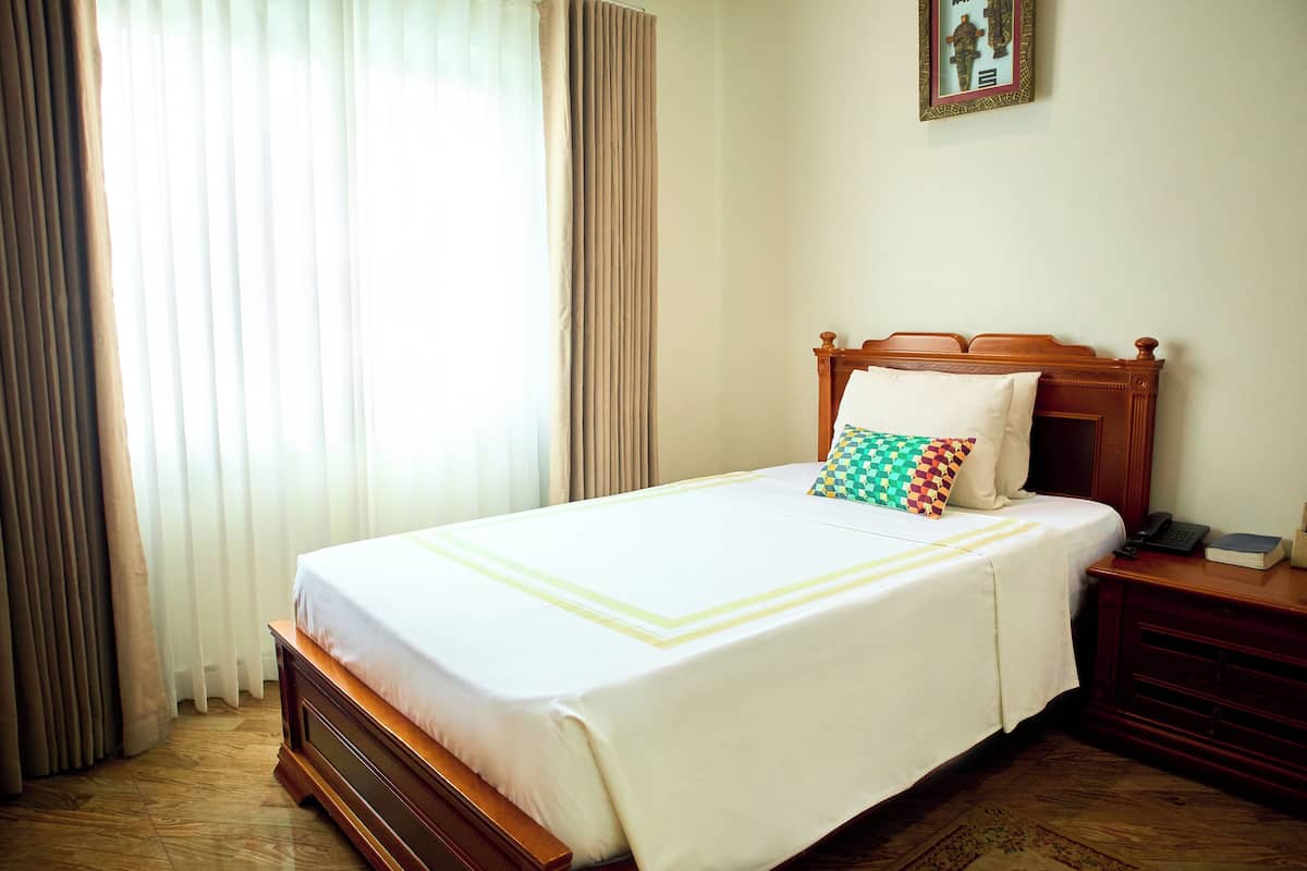 A neatly made bed with a white bedspread and two pillows, a wooden nightstand with a phone and book, and a framed picture on the wall.