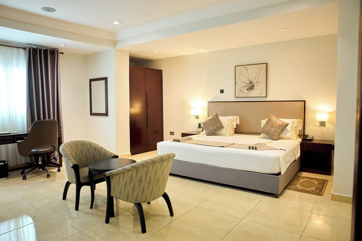A hotel room with a large bed, two chairs, a desk, and a nightstand with a lamp.