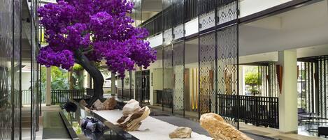 A modern indoor atrium with a central rock garden, a large purple flowering tree, and a reflective water feature.