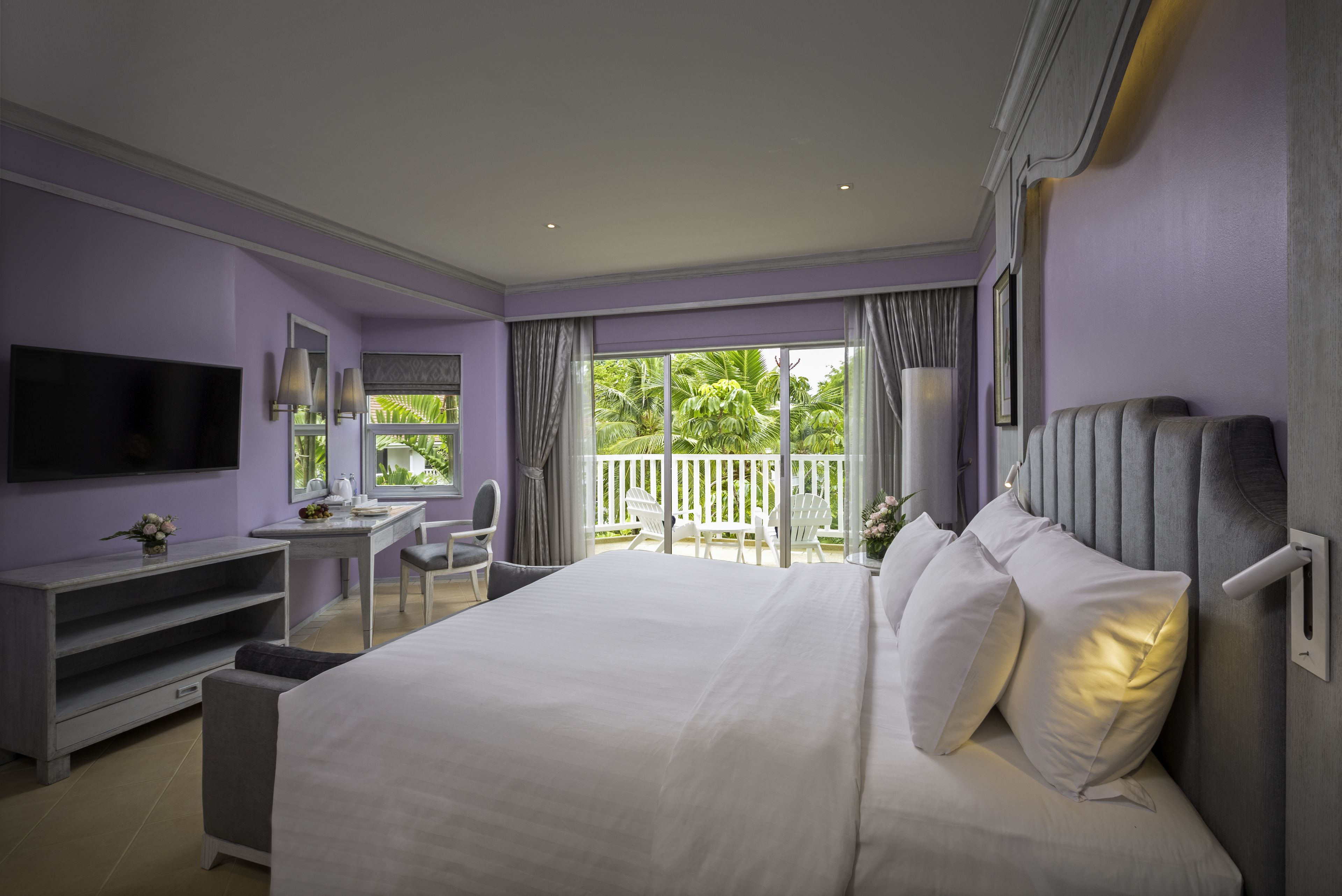 Ein modernes Hotelzimmer mit einem großen Bett, einem Schreibtisch, einem Fernseher und einem Balkon mit Blick auf Grünflächen.