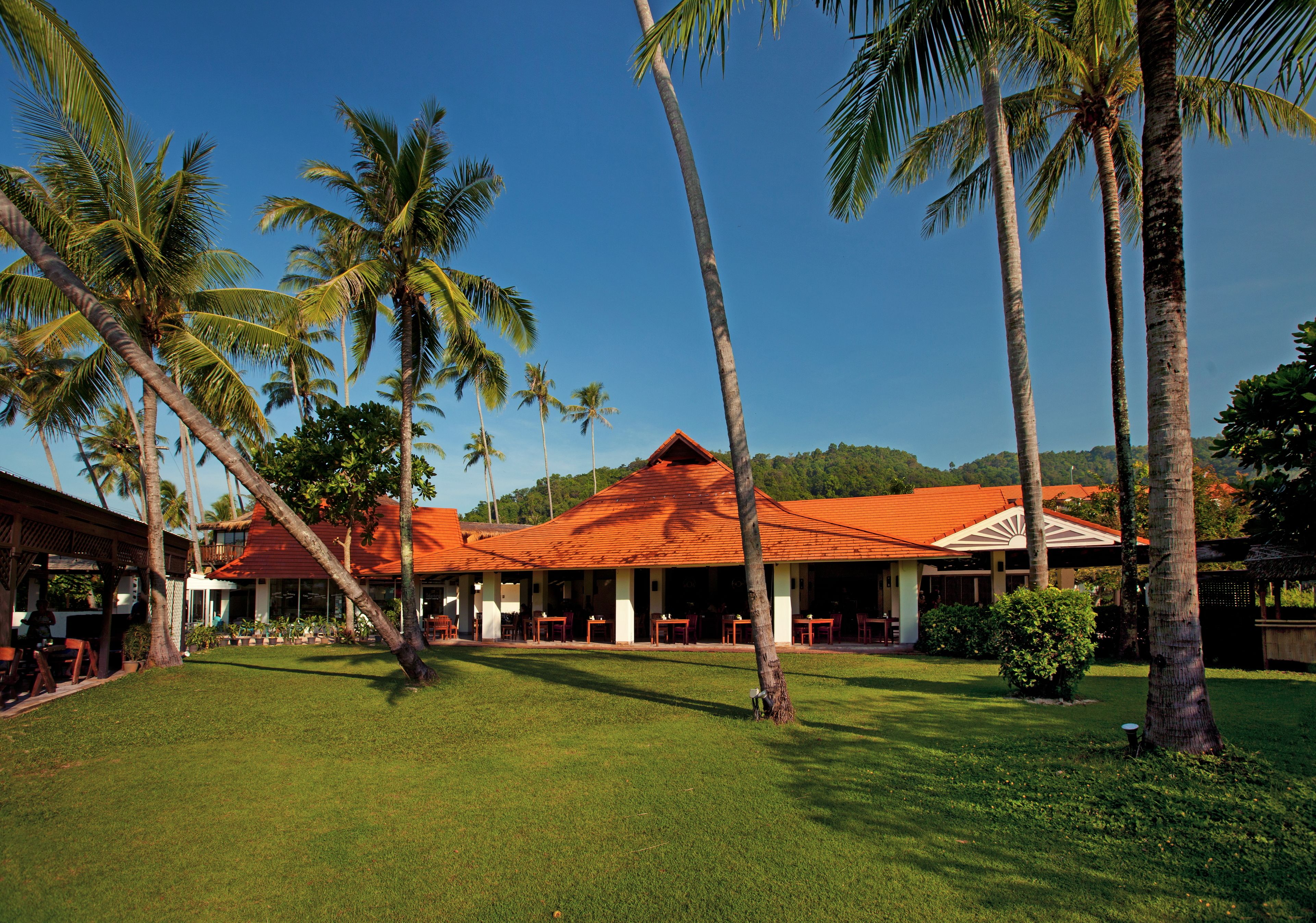 A resort with a red-roofed building, palm trees, and a grassy lawn.