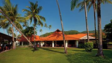 A resort with a red-roofed building, palm trees, and a grassy lawn.