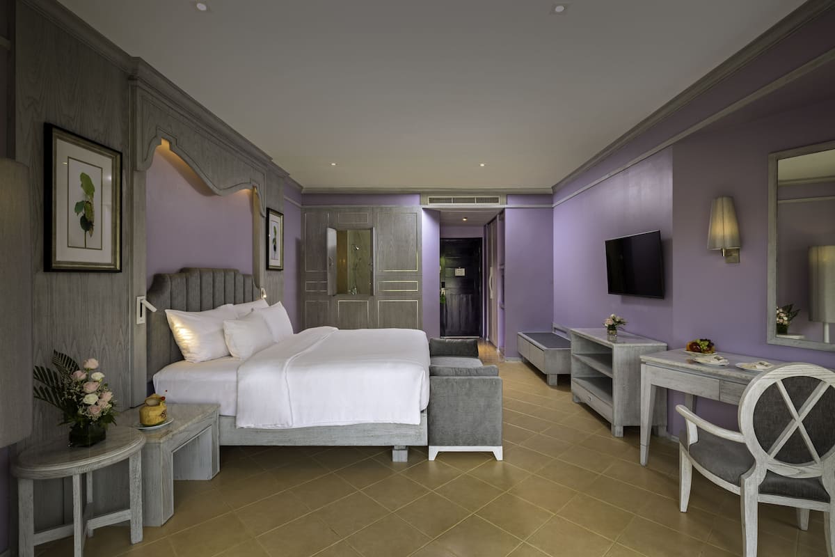 A modern hotel room with a bed, a desk, a chair, a TV, and a bathroom visible through an open door.