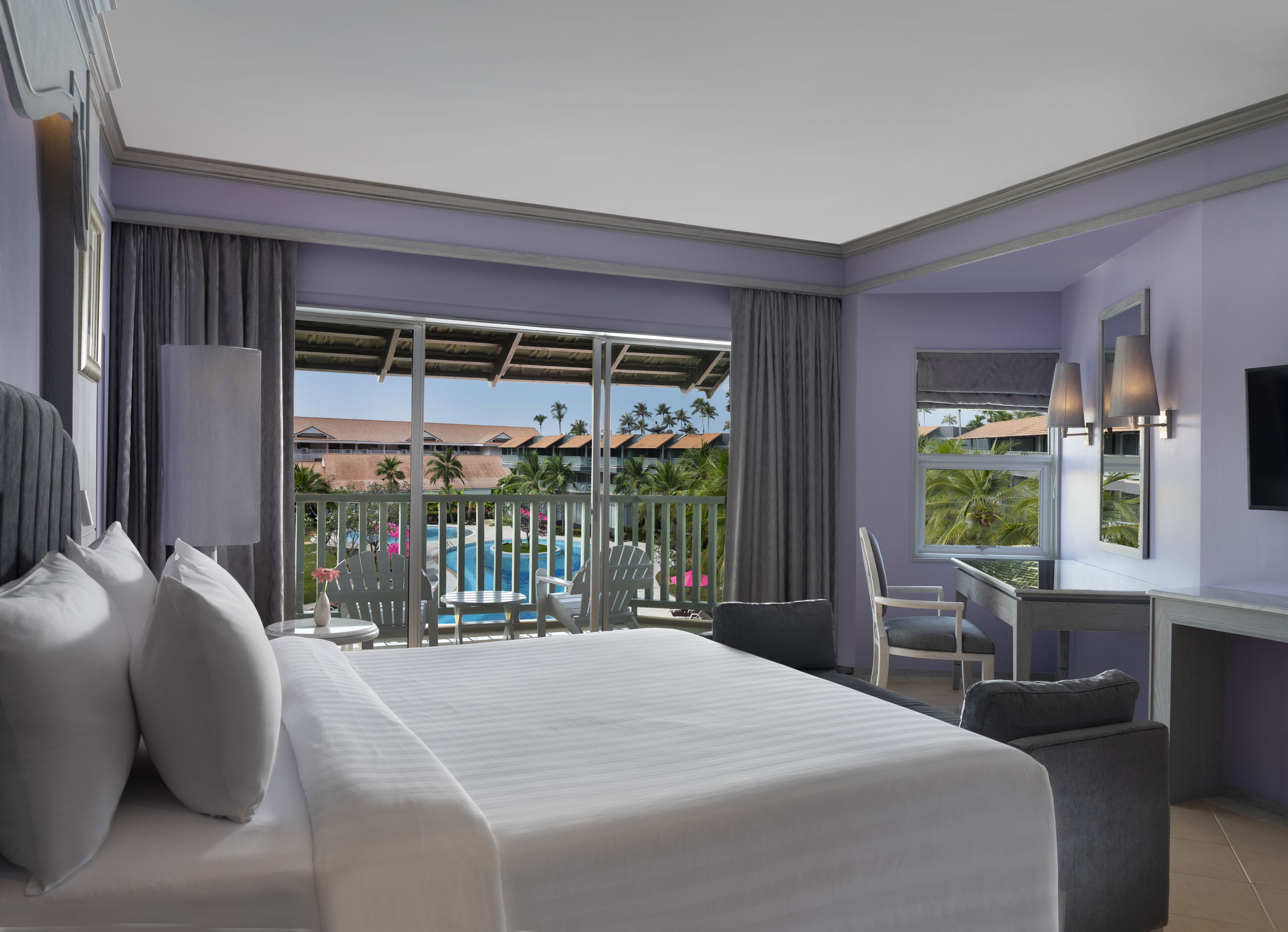 A hotel room with a large bed, a desk, and a view of a pool and palm trees.
