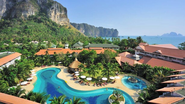 Un resort con una grande piscina, spiaggia e vista sul mare e sulle montagne.