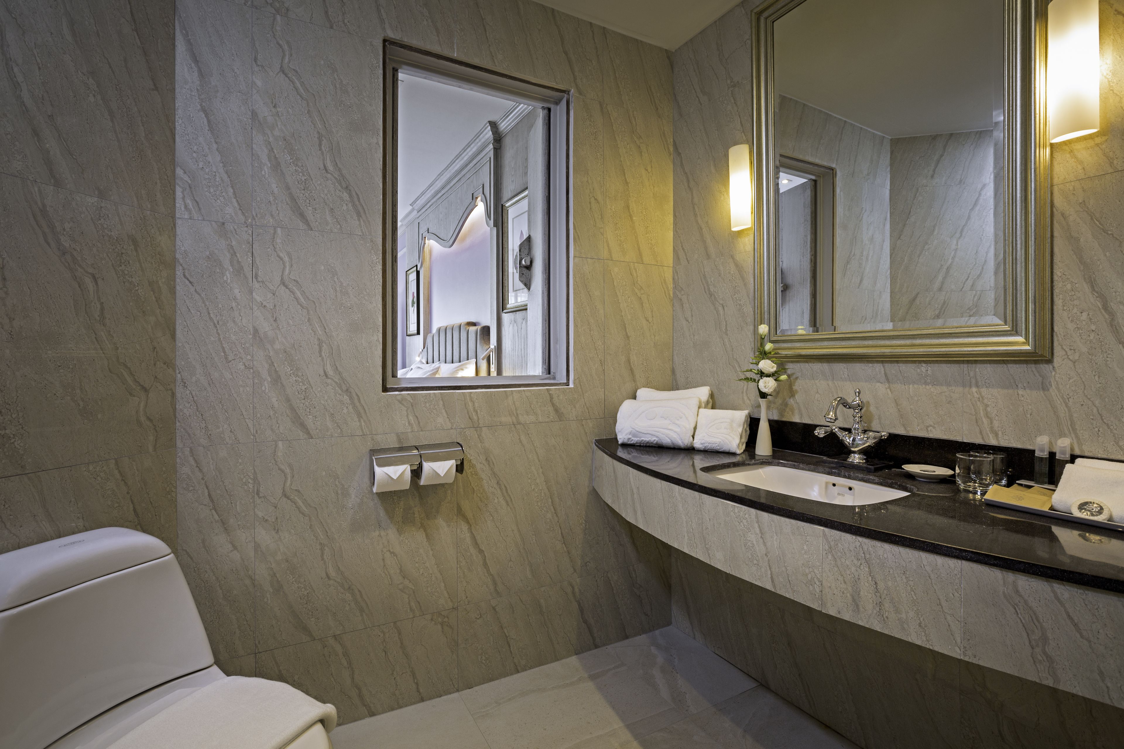 Een moderne badkamer met een marmeren wand, een grote spiegel, een wastafel en een toilet.