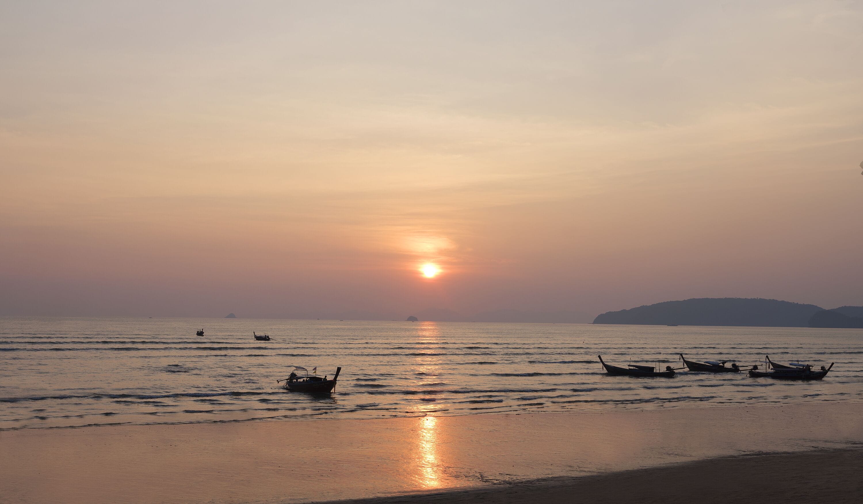 Atardecer sobre un mar tranquilo con varias embarcaciones ancladas.