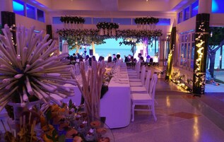 Un salón de banquetes con una larga mesa dispuesta para un evento formal, decorado con arreglos florales e iluminación.