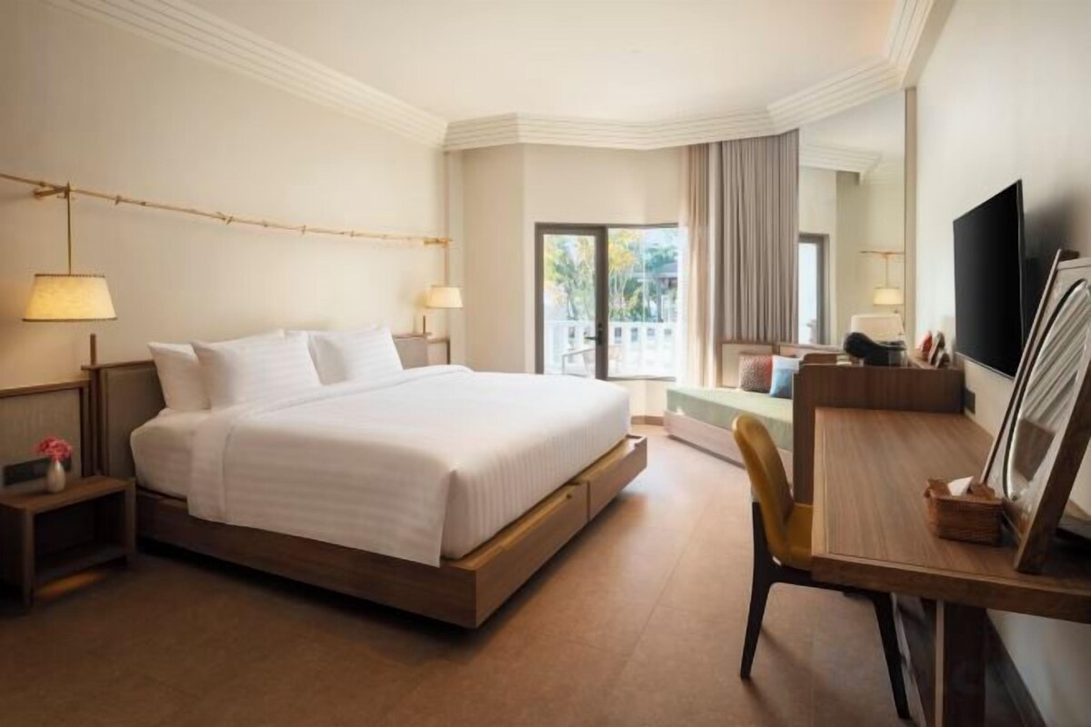 A hotel room with a bed, bedside tables, a desk with a chair, a television, and a window with curtains.
