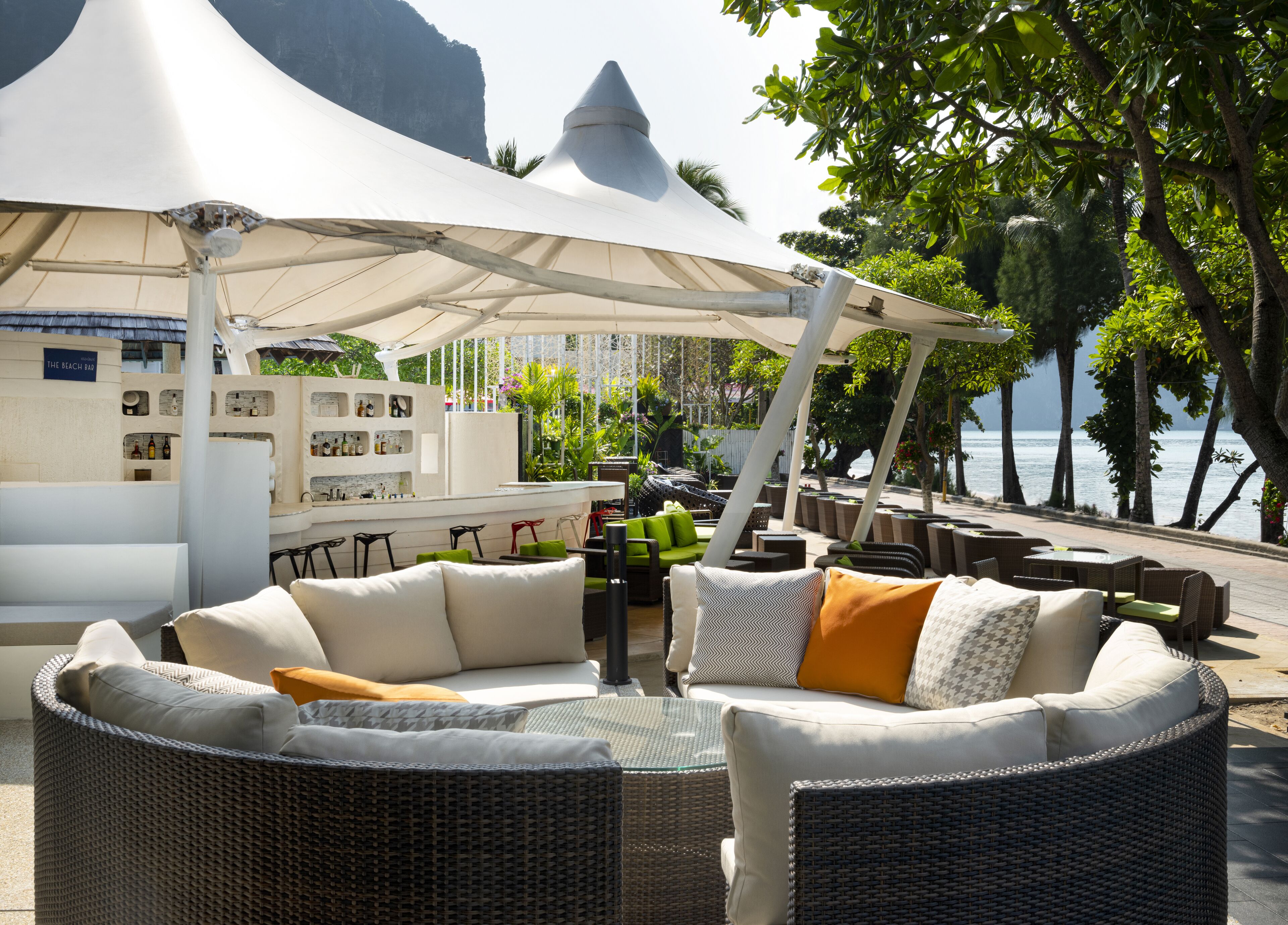 A beach bar with wicker furniture and a white canopy, overlooking the sea.