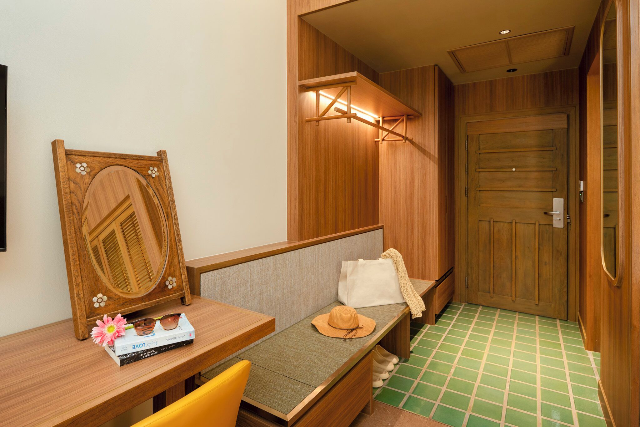 A room with a wooden bench, a small table with a book and sunglasses, and a door with a light fixture above it.