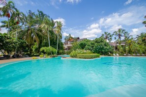 Una piscina amplia y cristalina rodeada de palmeras y sillones de descanso.