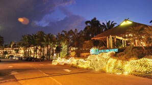 Een resort met een bord waarop 'ELIX RIVER KWAI RESORT' staat, en een goed verlicht entreegebied met palmbomen en sfeerverlichting.