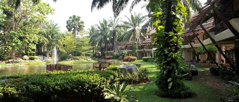 A lush garden with a pond, palm trees, and a waterfall.