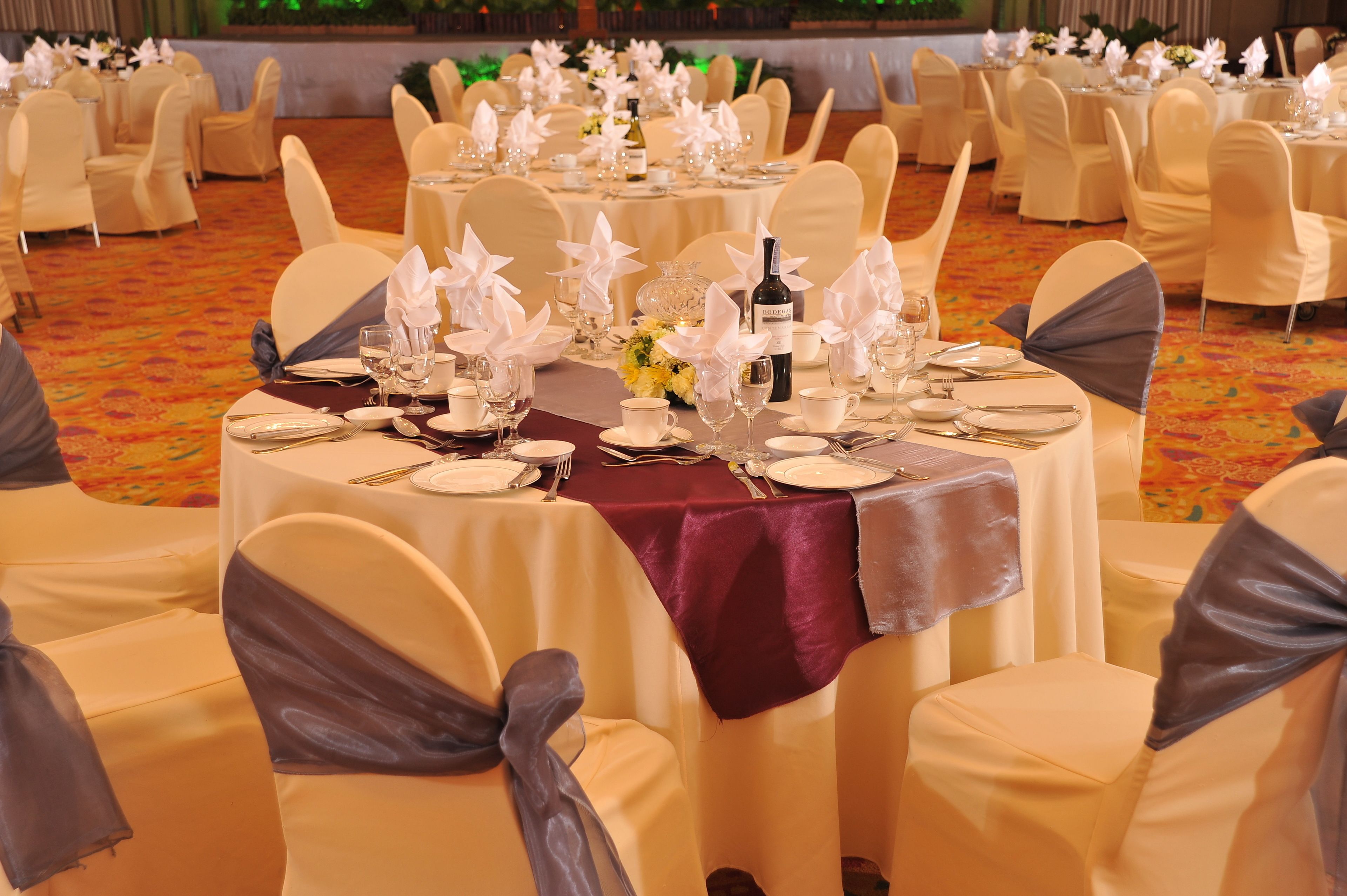 A banquet hall with round tables set for a formal event, each with white tablecloths, silverware, and glassware.