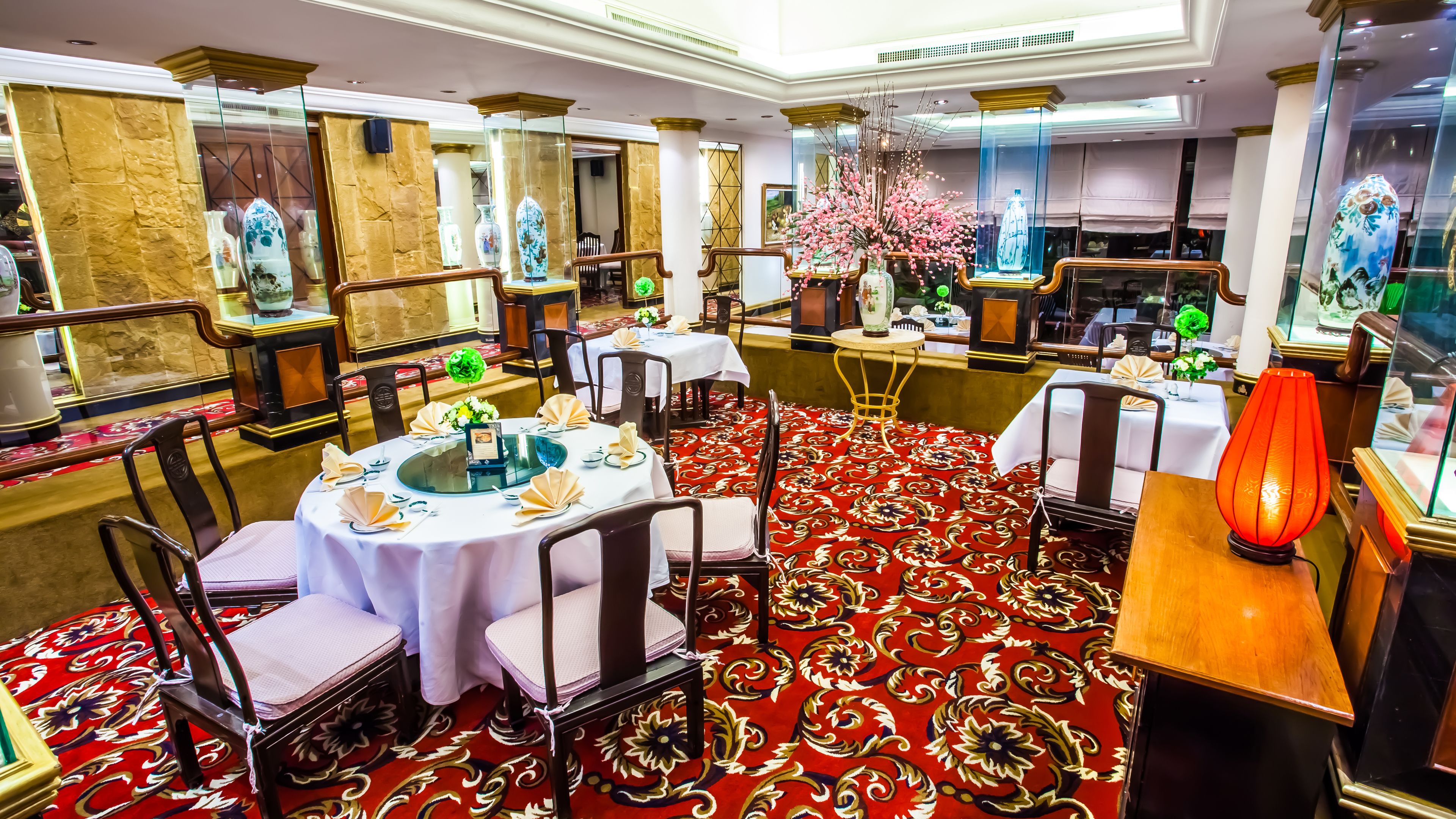 A dining area with round tables, chairs, and a red patterned carpet.