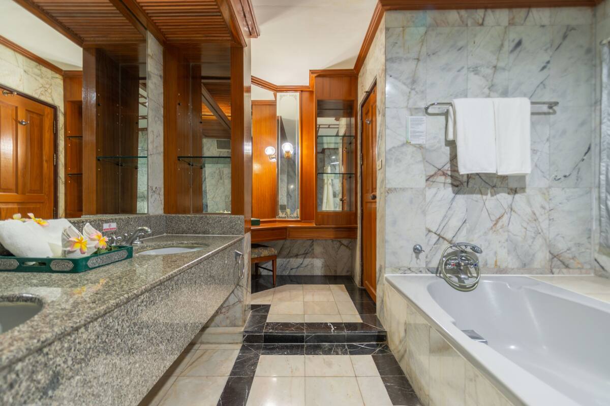 Ein modernes Badezimmer mit Marmorboden, einer Badewanne, einem Waschbecken mit Glasabtrennung und Holzschränken.