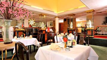 Un restaurante con varias mesas dispuestas para comer, con manteles blancos y platos ordenados.