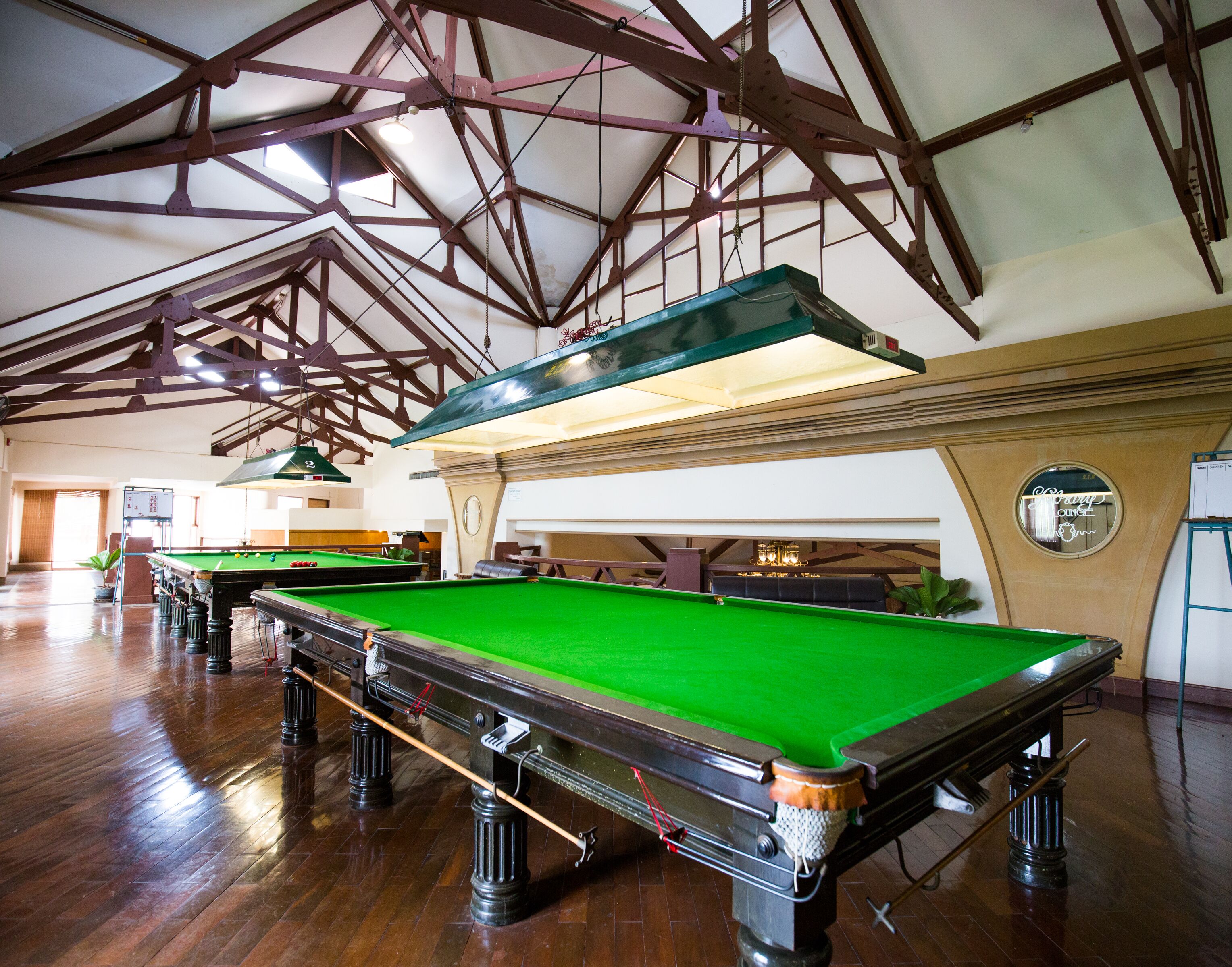 A billiards hall with multiple tables, wooden flooring, and a high ceiling with exposed beams.