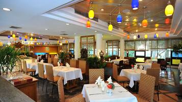 A restaurant with multiple tables and chairs, a bar area, and a view of the outdoors through large windows.