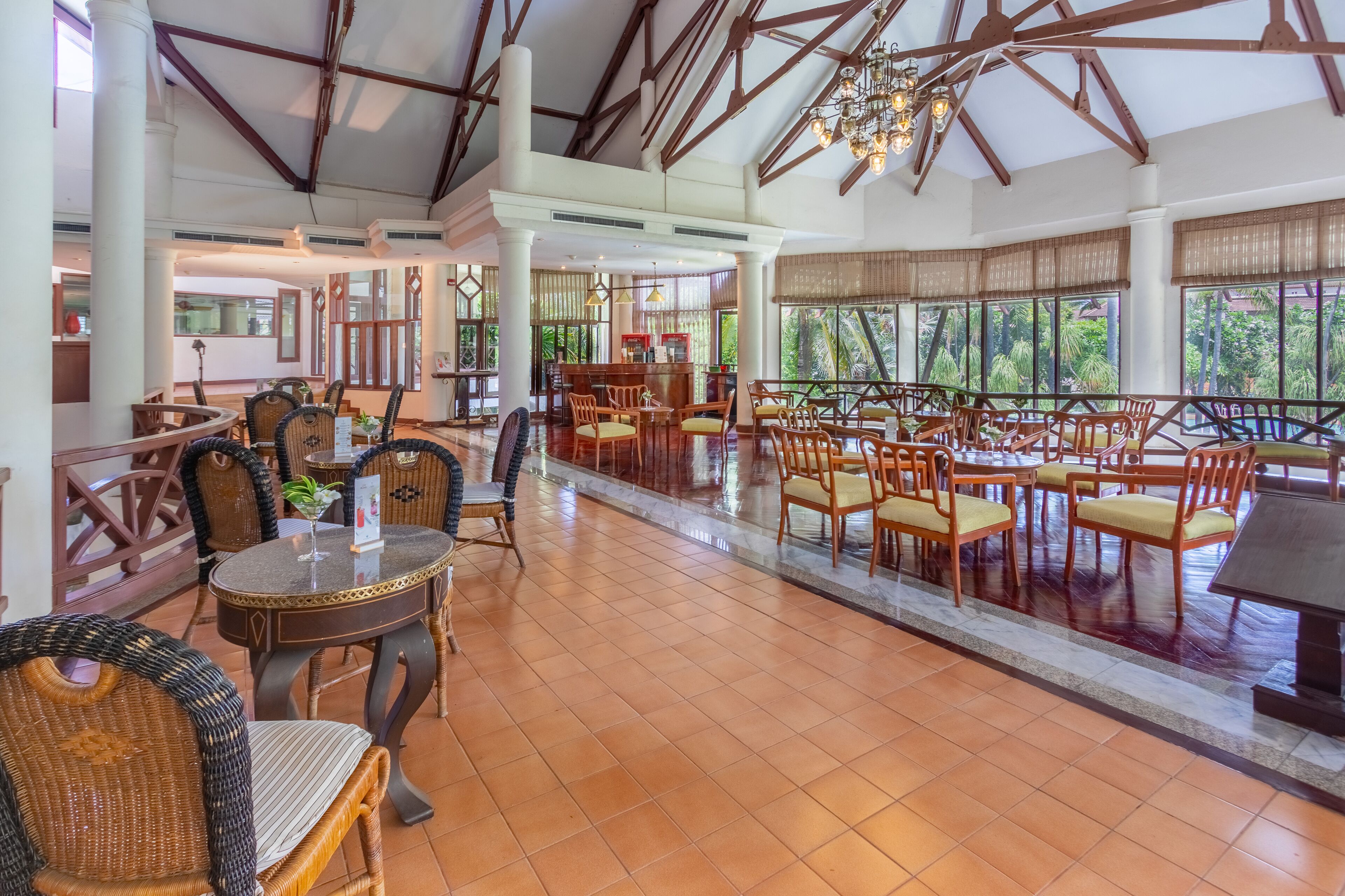 A spacious indoor area with multiple seating arrangements, including round tables and chairs, and large windows providing views of the outdoors.