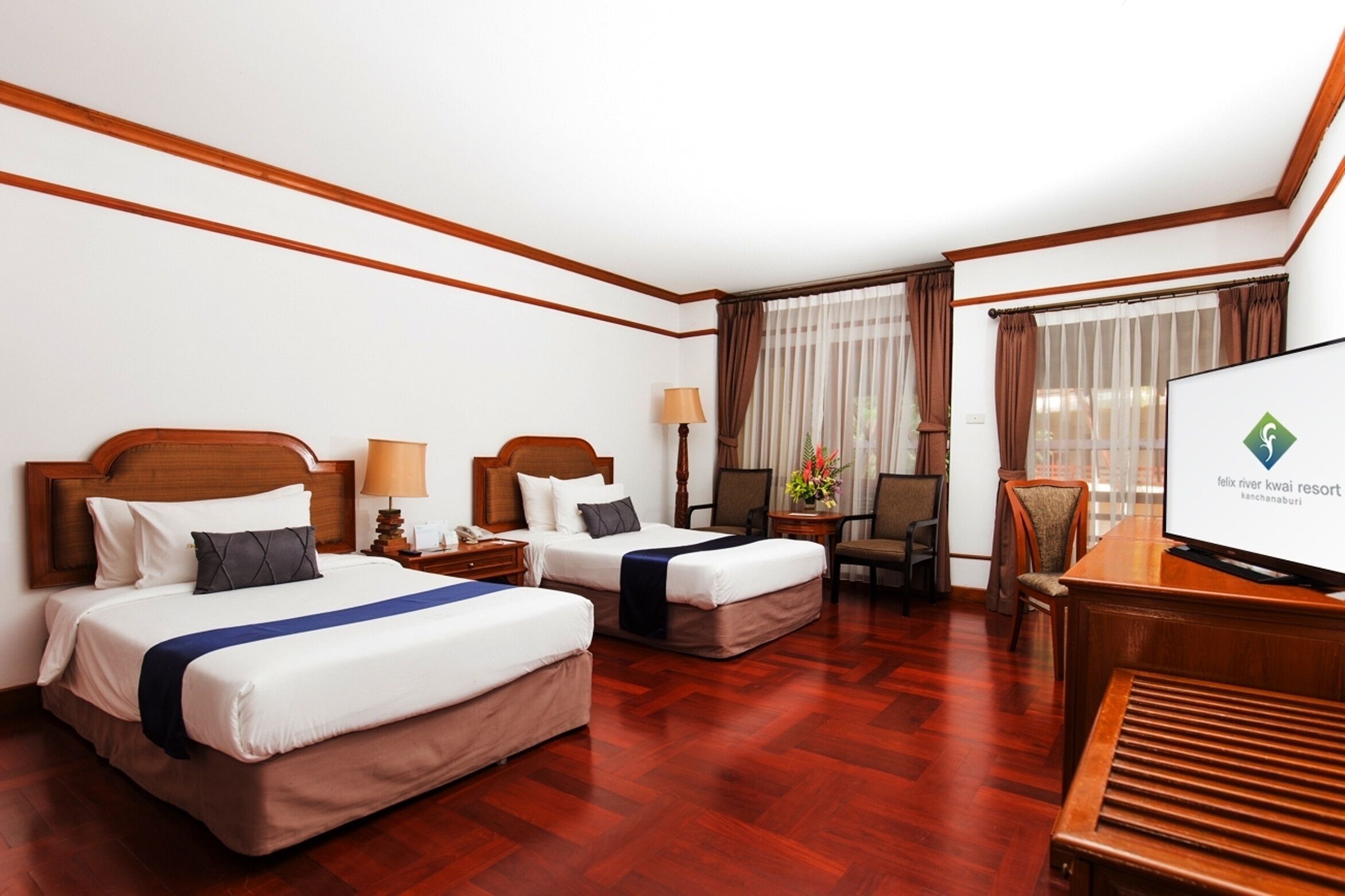 A hotel room with two beds, a desk, a television, and a window with curtains.