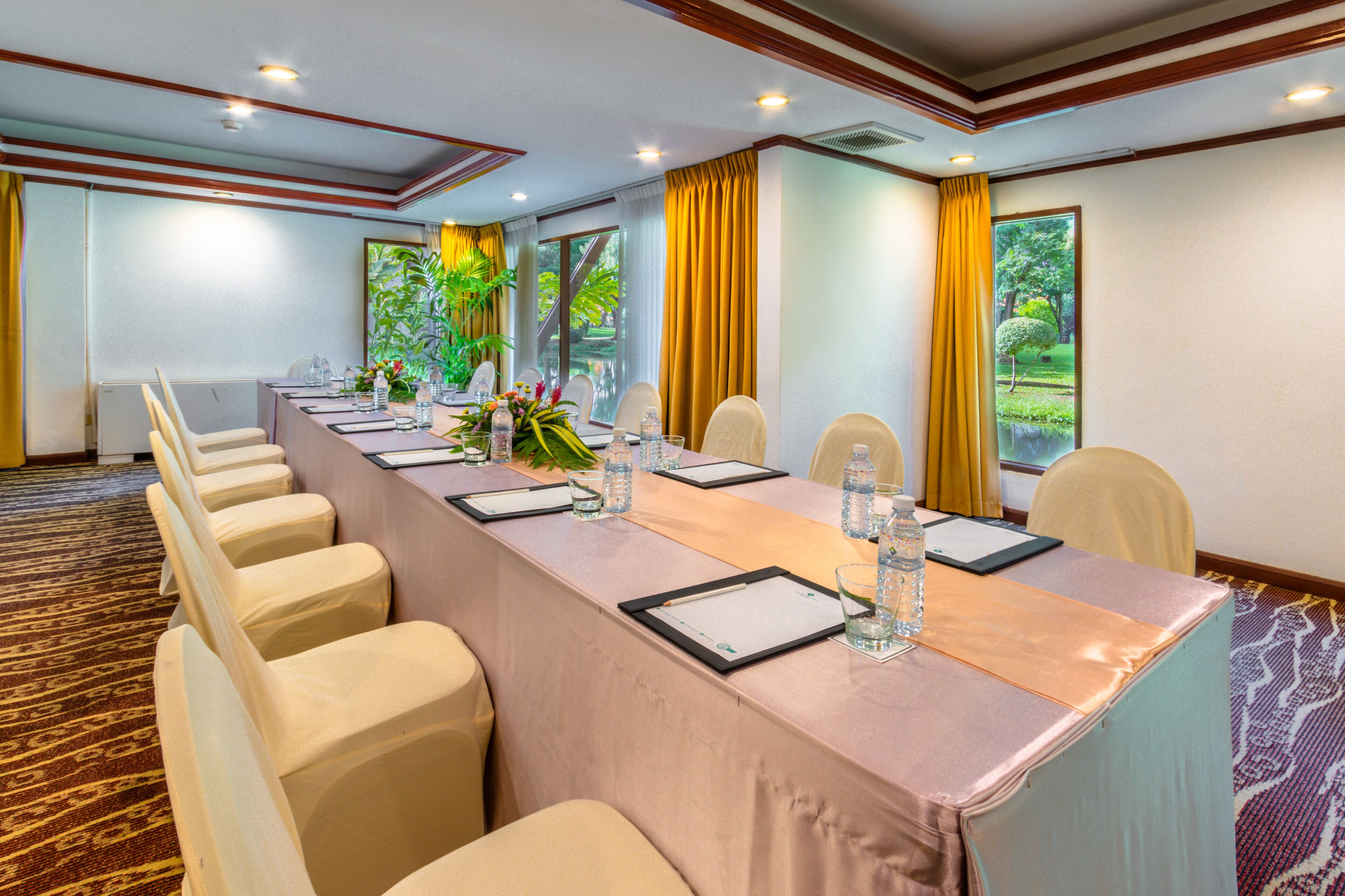 A conference room with a long table, chairs, and a view of greenery through large windows.