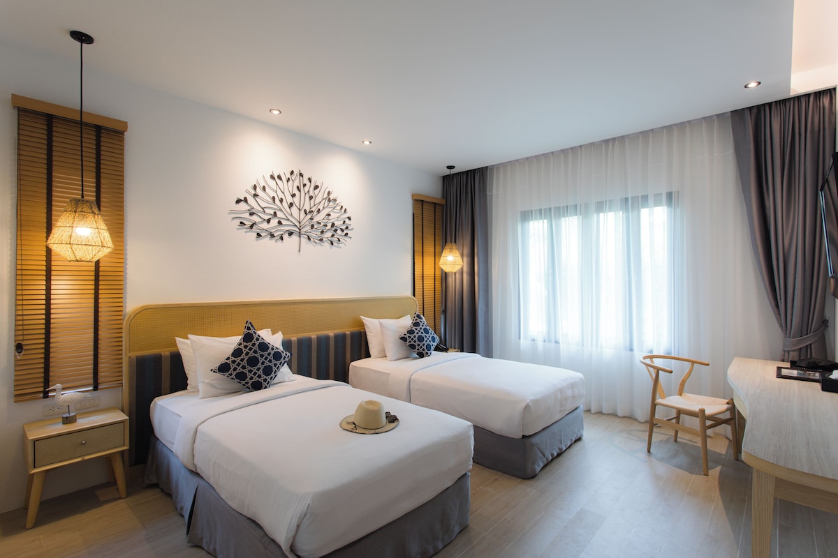 Habitación de hotel con dos camas, un escritorio, una silla, un adorno de pared y una ventana con cortinas.