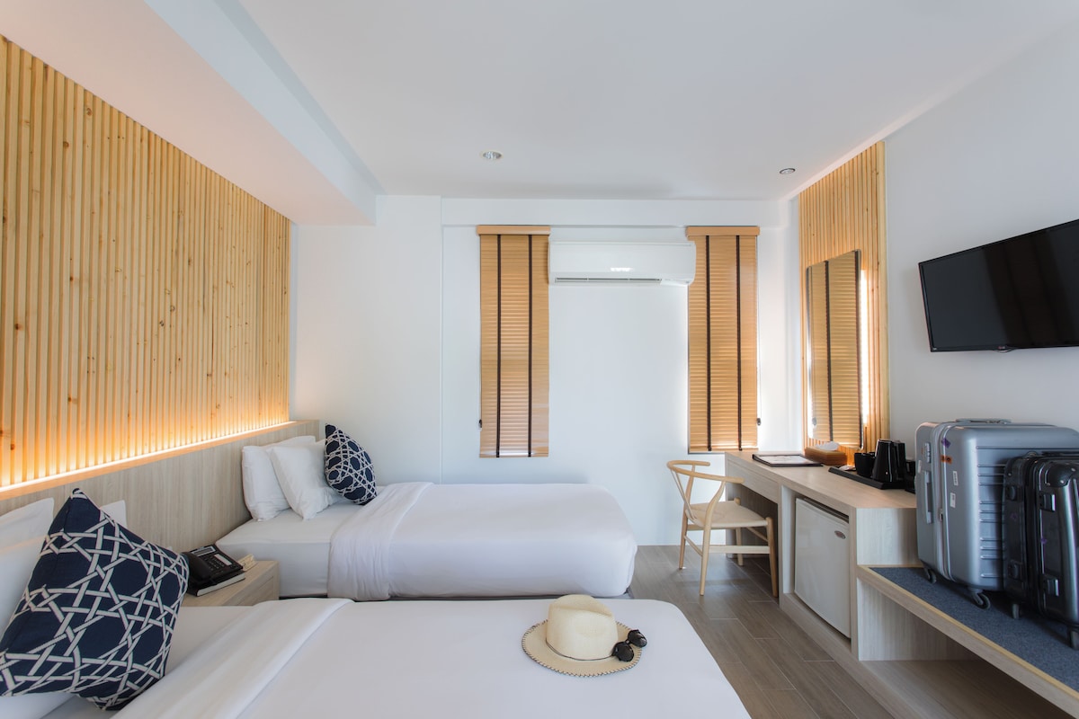 Habitación de hotel con cama, mesita de noche, escritorio con silla, televisor de pantalla plana y perchero para equipaje.