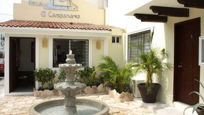 A hotel entrance with a fountain, potted plants, and a tiled roof.