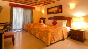 A hotel room with a wooden ceiling, a bed with a red and white headboard, a bedside table with a lamp, and a chair.