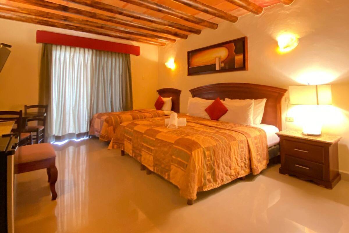 Una habitación de hotel con techo de madera, una cama con cabecera roja y blanca, una mesita de noche con lámpara y una silla.