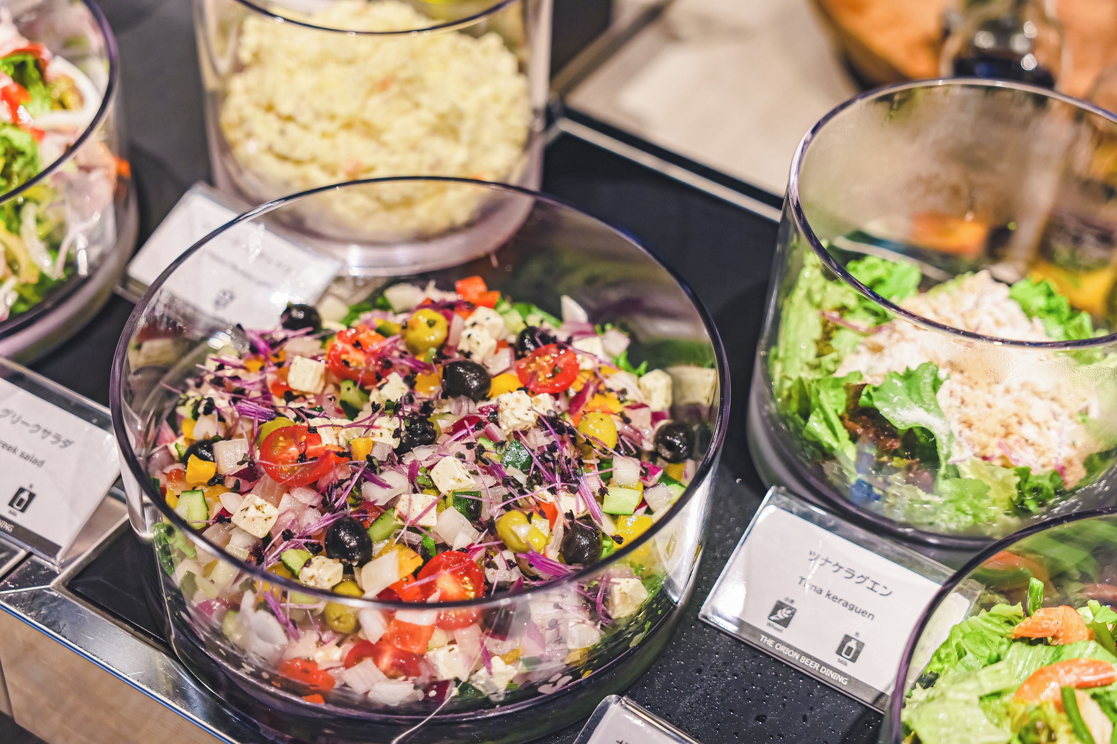 A buffet with various salads and a container of mashed potatoes.