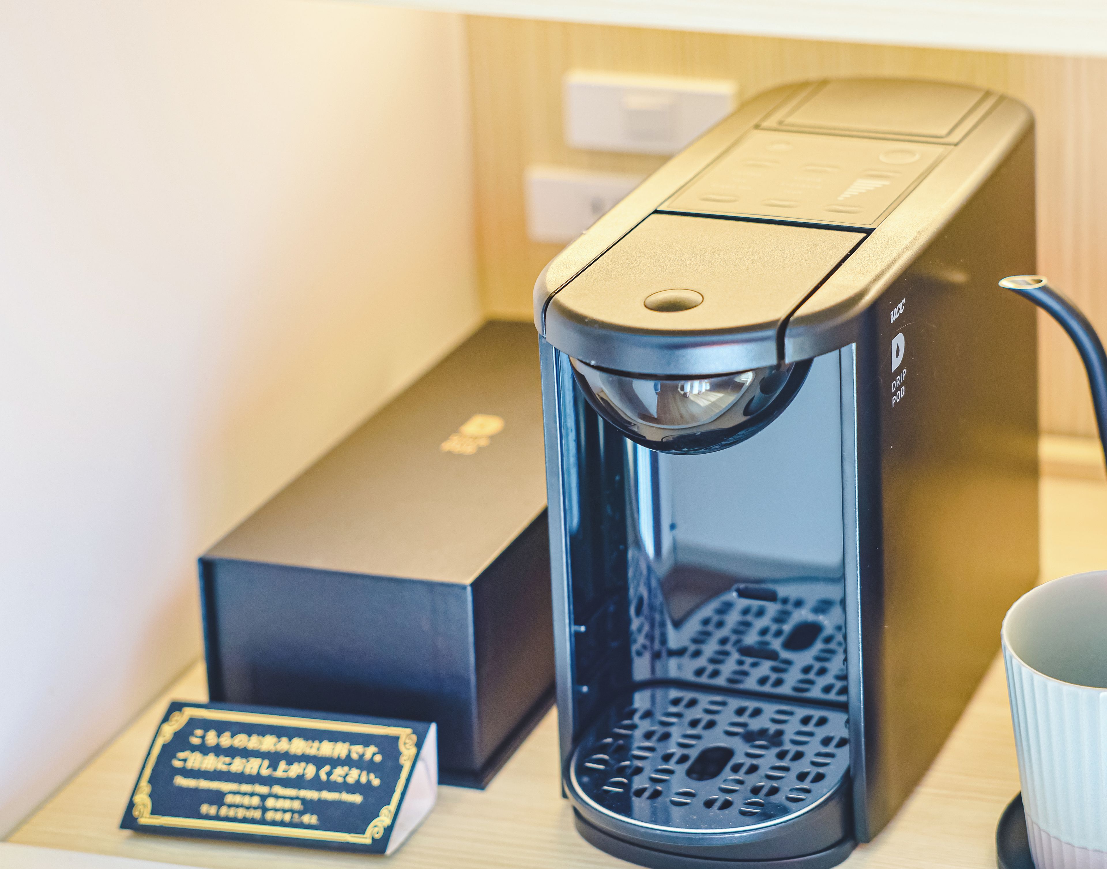 Una cafetera con una bandeja de goteo, una caja y una taza sobre una mesa.