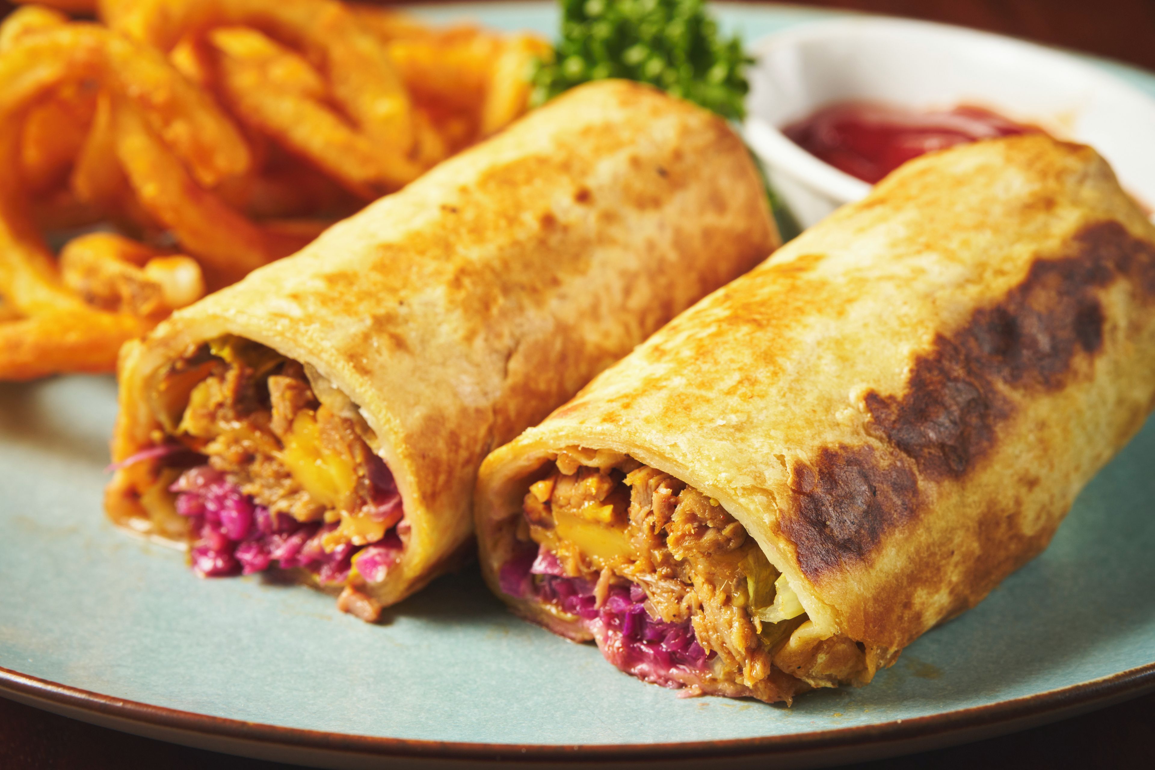 Un plato con un burrito, una porción de papas fritas y un recipiente pequeño de salsa.