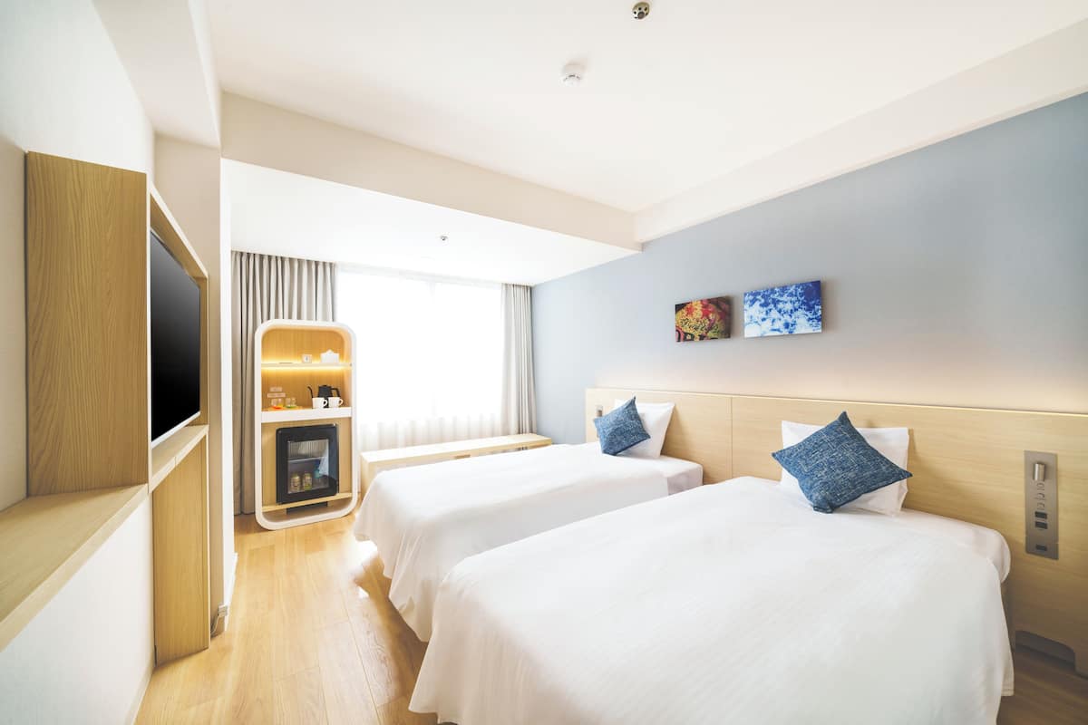 A hotel room with two beds, a TV, a minibar, and artwork on the wall.