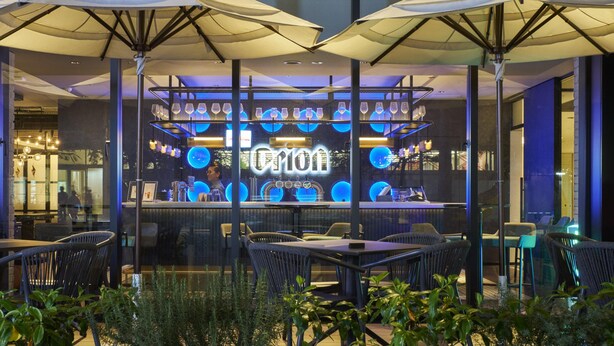 An outdoor seating area with tables and chairs, umbrellas, and a bar with a glass display.