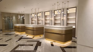 A modern reception area with three counter stations, each with a marble top and gold accents. Overhead, there are multiple spherical pendant lights. The floor is tiled with a geometric pattern.