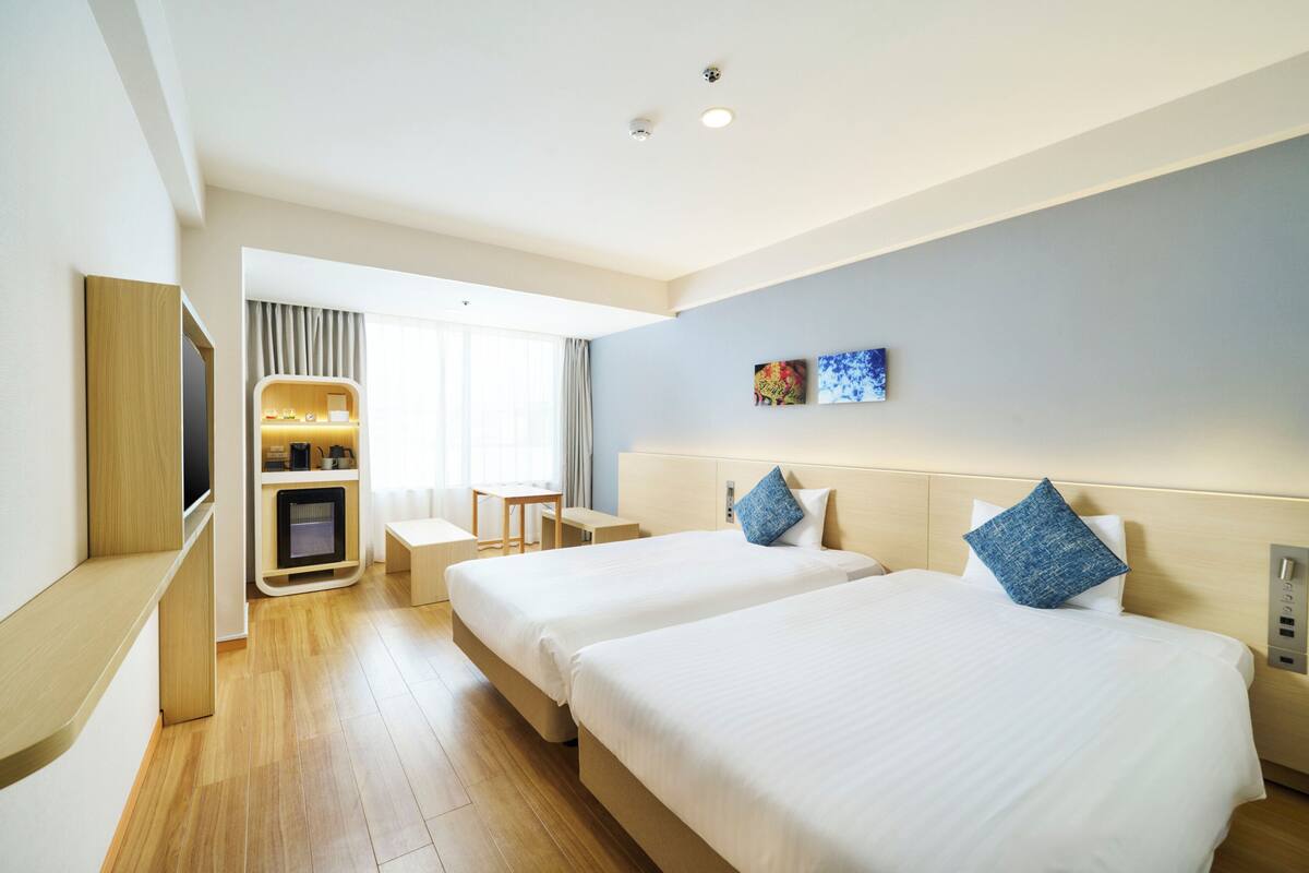 A hotel room with two beds, a desk, a TV, and a small seating area.
