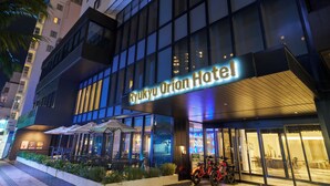 The Ryukyu Orion Hotel exterior at night with illuminated signage, outdoor seating, and a red bicycle parked outside.