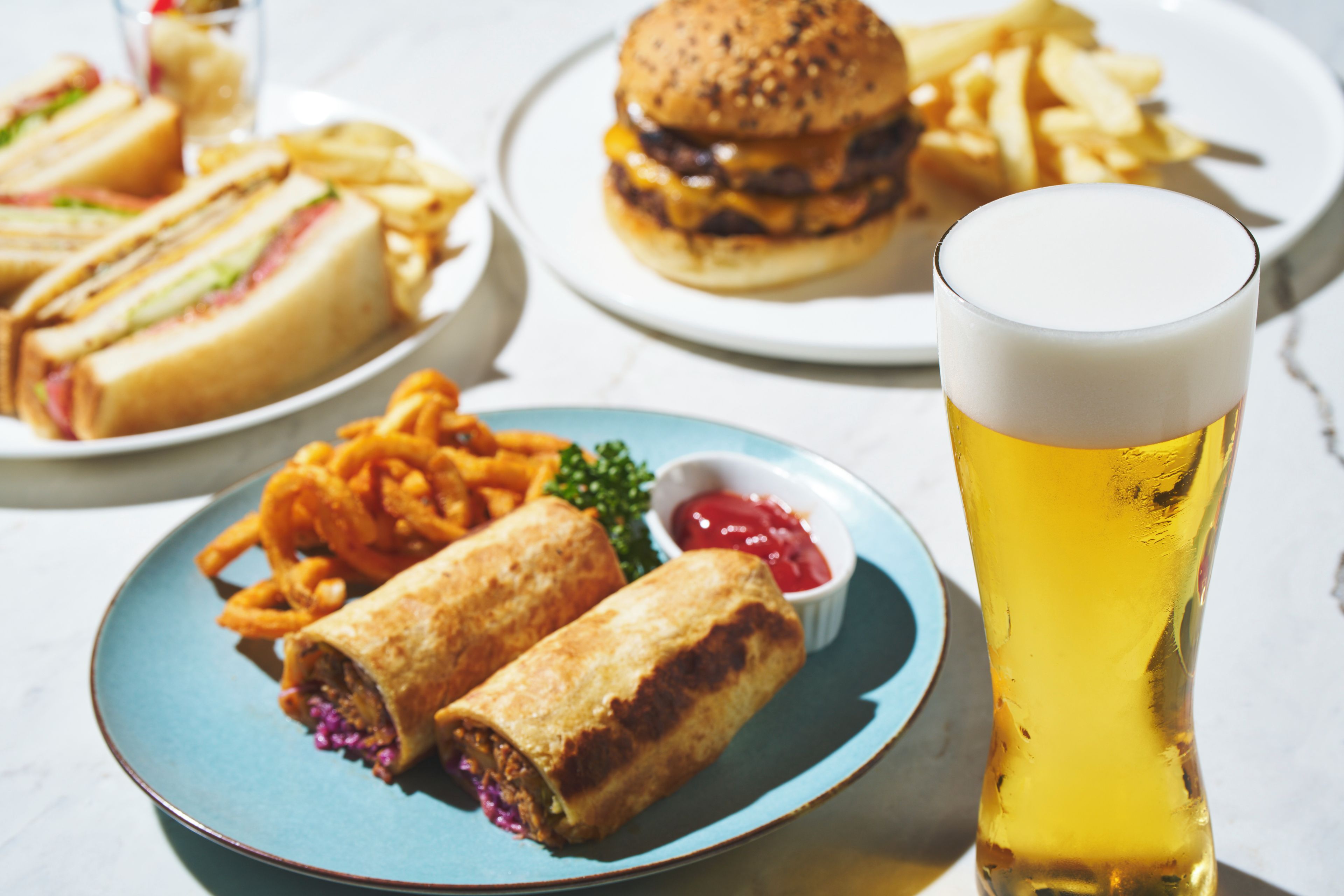A meal consisting of a sandwich, fries, a burger, and a glass of beer.