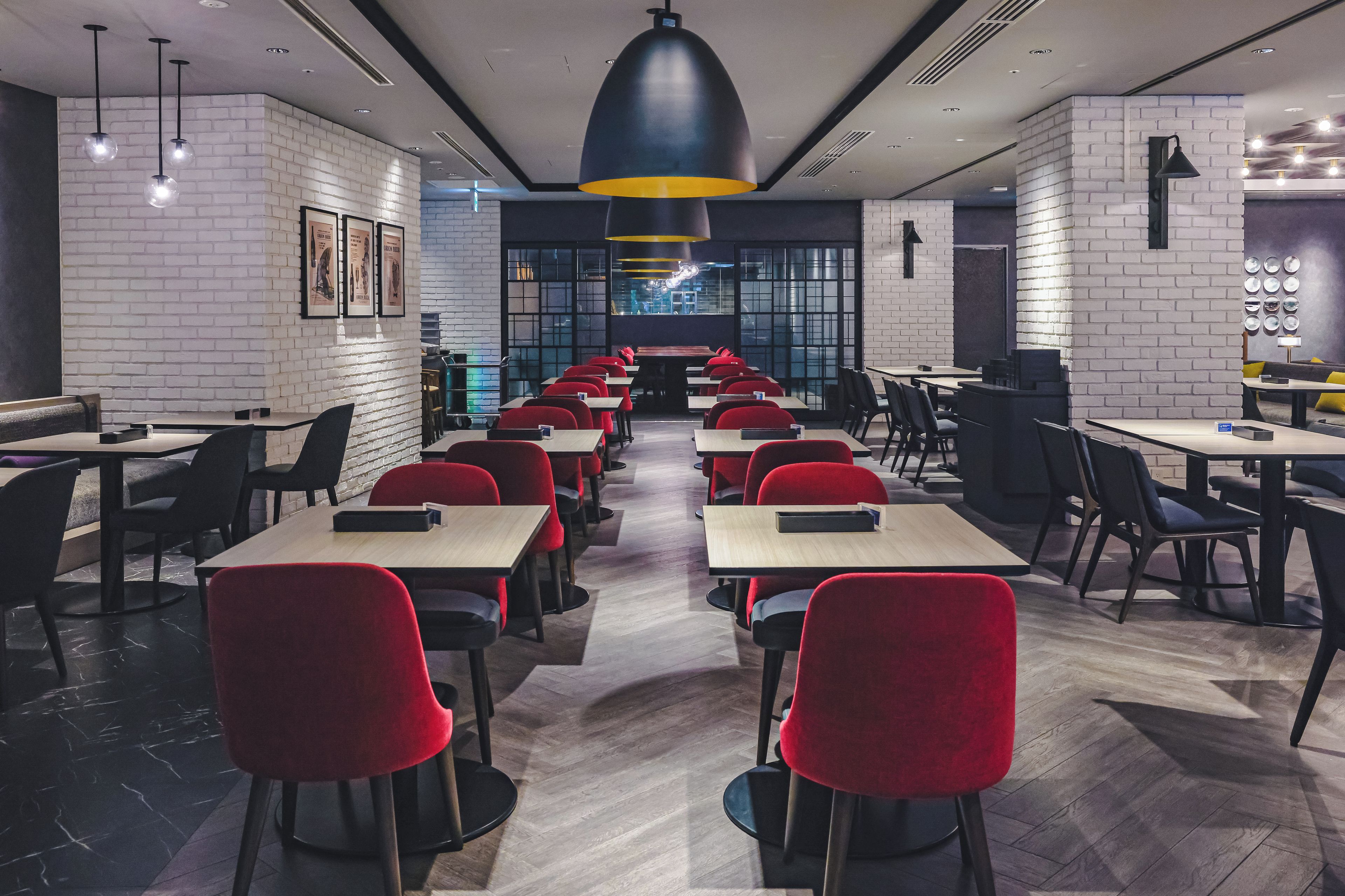 Ein modernes Restaurant mit langen Tischen, roten Stühlen und Pendelleuchten.