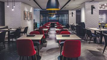 Ein modernes Restaurant mit langen Tischen, roten Stühlen und Pendelleuchten.