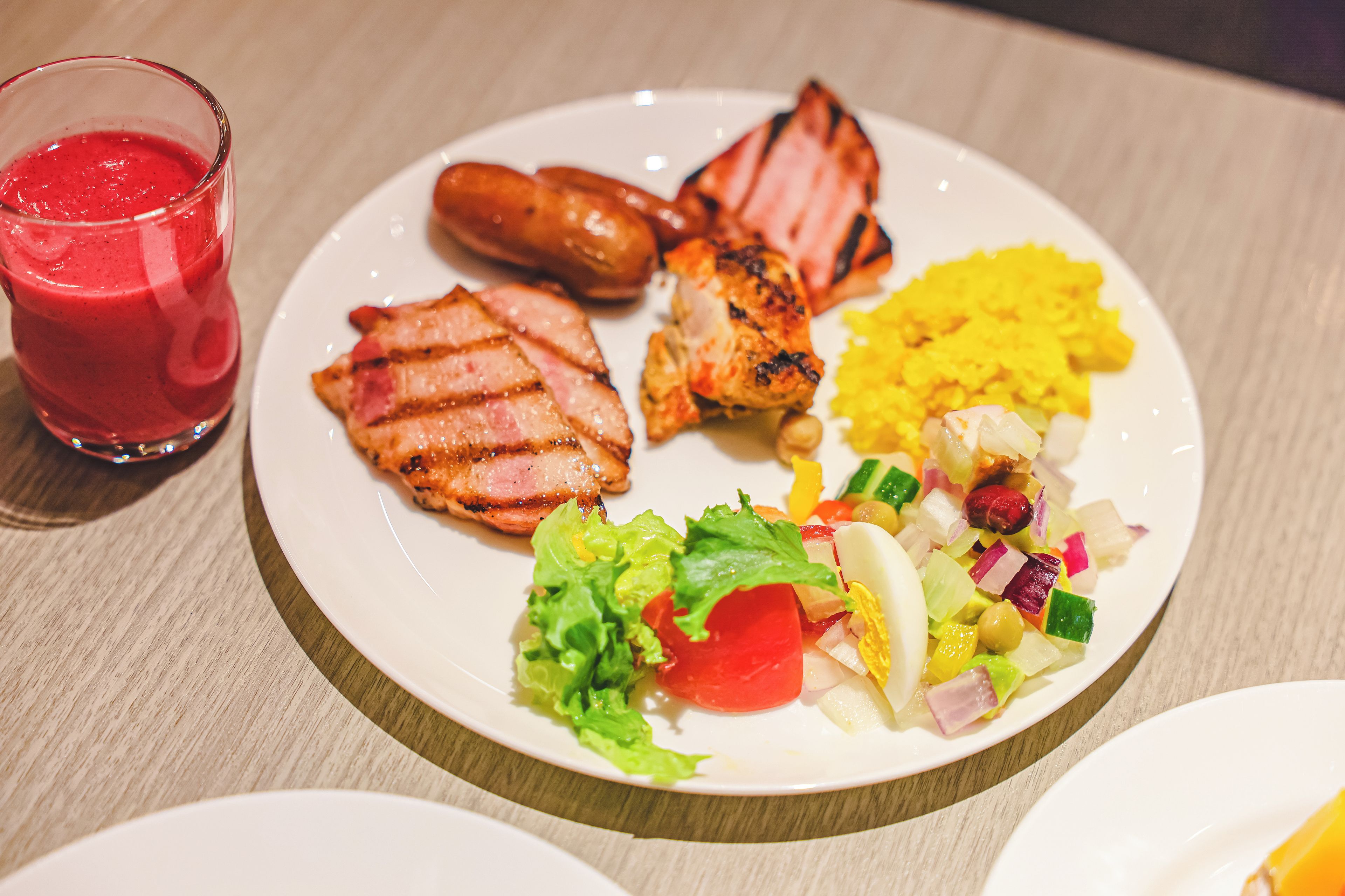 Un plato de comida con carne a la parrilla, salchichas y una ensalada de verduras variadas.